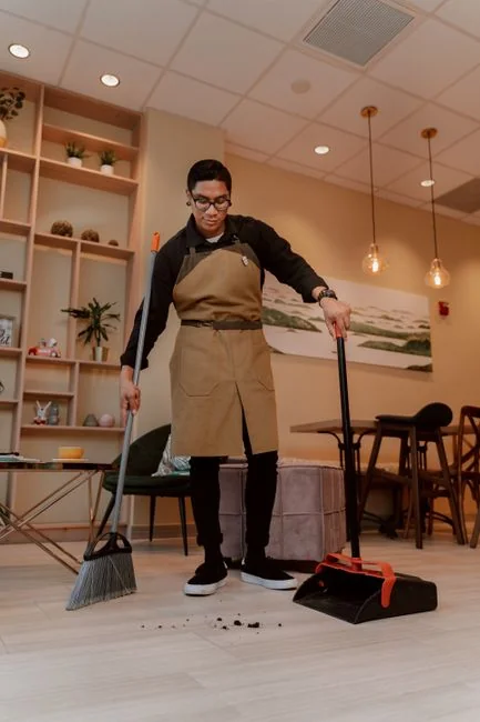 Gros plan d’une main nettoyant une fenêtre à l’extérieur avec une raclette, en portant des gants jaunes.
